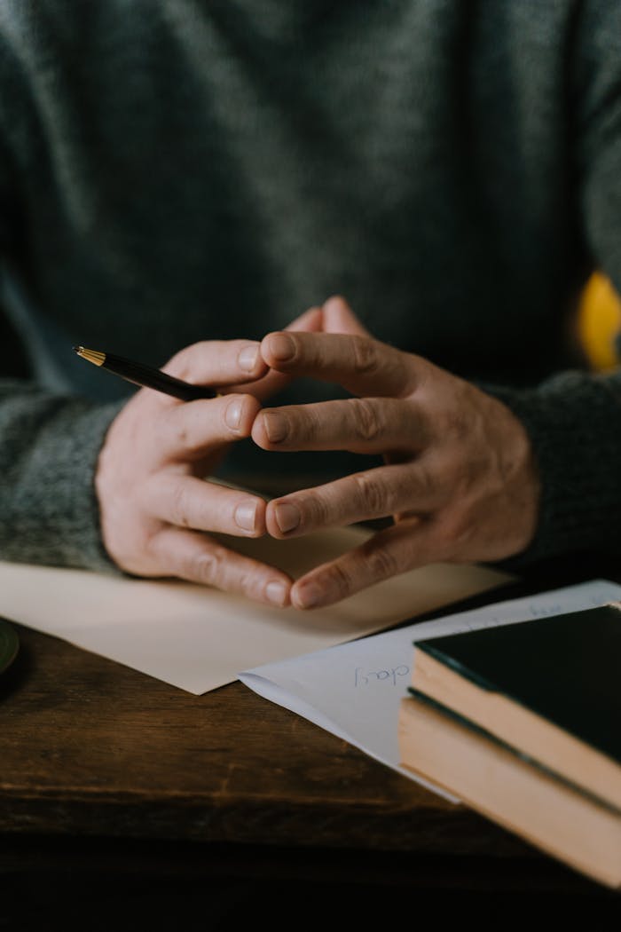 Close-up of hands with pen, capturing a thoughtful writing moment at a wooden table indoors.